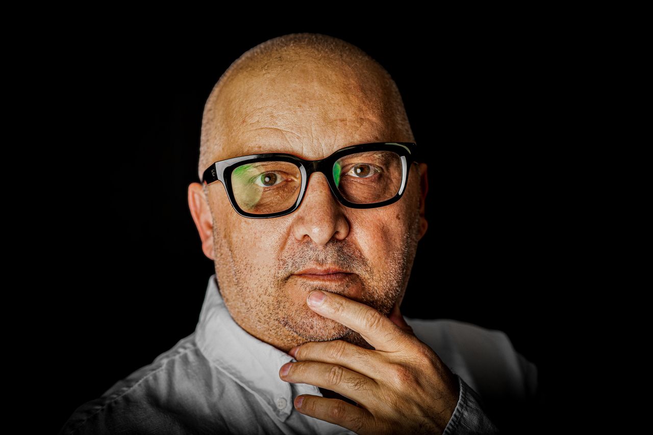 Close-up portrait of a thoughtful senior man with glasses against a black background.