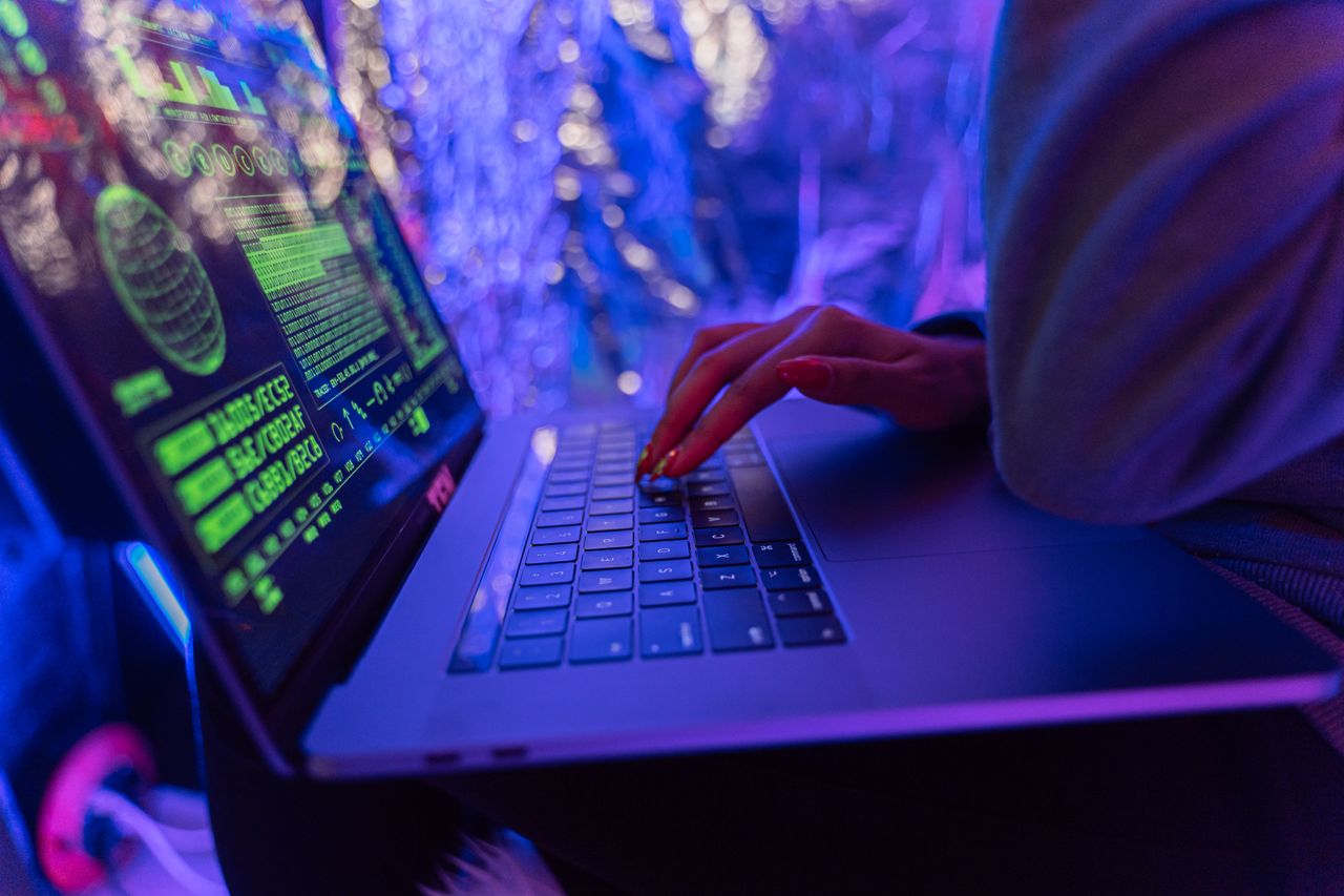 services-02 Close-up of hands typing on a laptop displaying cybersecurity graphics, illuminated by purple light.